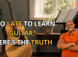 Thumbnail showing a smiling man in an orange polo, a guitar on the left, music stand with sheet music, and the text 'Too late to learn guitar? Here’s the truth' with a logo in the top-right corner.